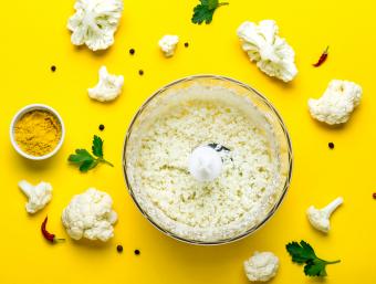 وعاء الخلاط مع أرز القرنبيط الطازج والتوابل على خلفية صفراء