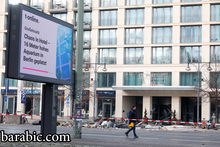 رجل يمشي أمام الأنقاض ولوحة إعلانية رقمية تعرض الأخبار في الشارع أمام فندق بعد انفجار ويهرب من أكوادوم أكواريوم